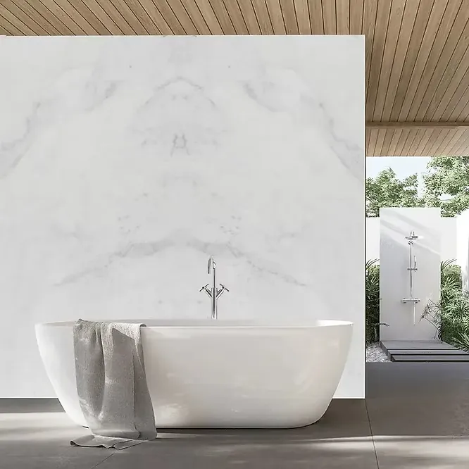 A minimalist contemporary bathroom featuring a freestanding white bathtub against a bookmatched white marble wall panel with soft, subtle veining.
