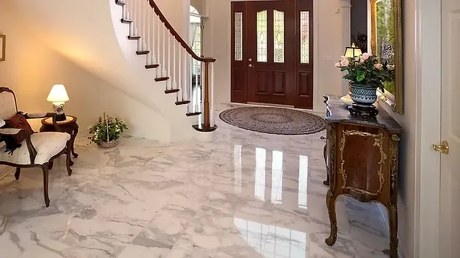 A classic, elegant home foyer showcasing highly polished white marble flooring with grey veining that reflects the warm indoor lighting.
