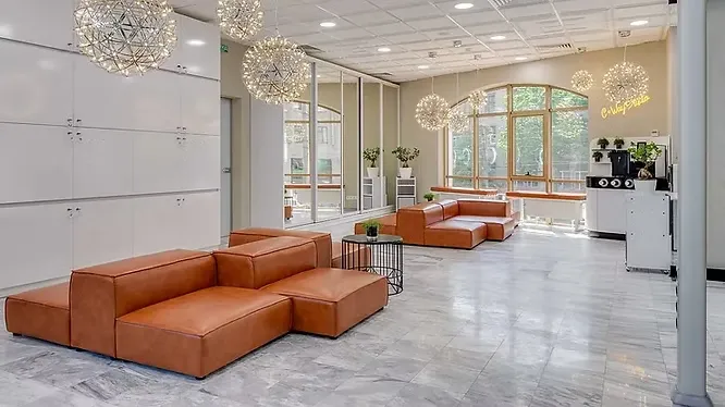 A spacious lobby with grey marble flooring, brown leather modular couches, and spherical wire lights.