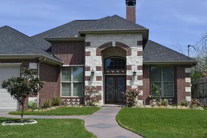 A classic suburban house with a red brick exterior accented by light stone details framing the grand arched entryway.