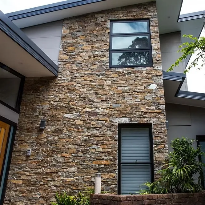 A contemporary architectural facade utilizing a textured multi-toned natural stone cladding wall around large minimalist windows.
