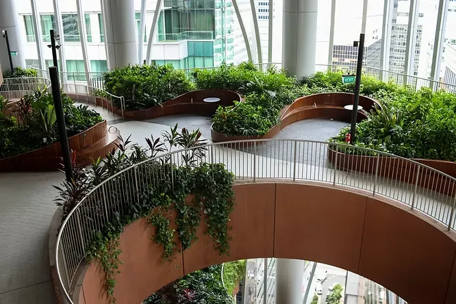 An elevated view of a multi-level indoor terrace within a skyscraper, showcasing curved planters filled with dense green foliage and integrated seating areas.