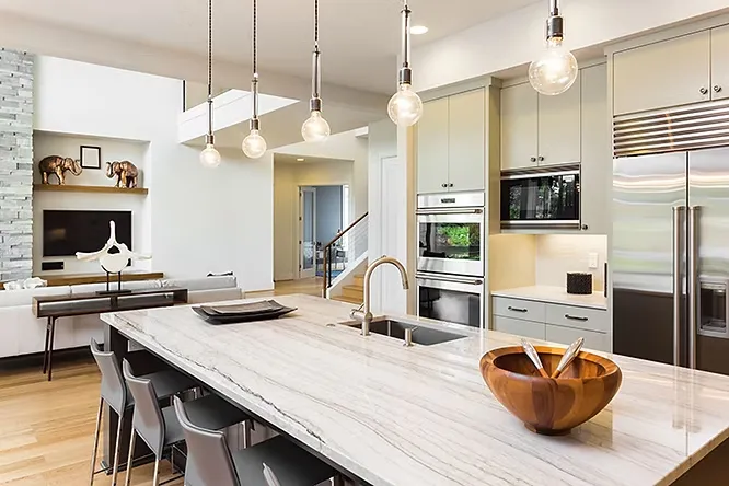 A modern kitchen space showcasing a large central island with a dramatic, subtly-veined white stone countertop under hanging pendant lights.