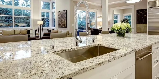 A spacious kitchen showing a polished granite countertop with a speckled gray and white pattern surrounding a stainless steel sink.