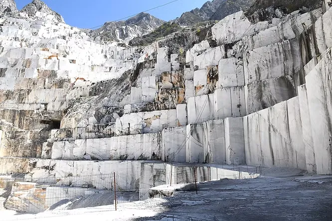 A breathtaking view of a massive white marble quarry sliced into steep, geometric terraces high up in the mountains.