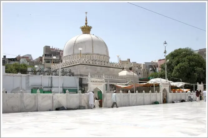 The iconic white dome and marble courtyard of the historic Ajmer Sharif Dargah stand peaceful under a bright afternoon sky.