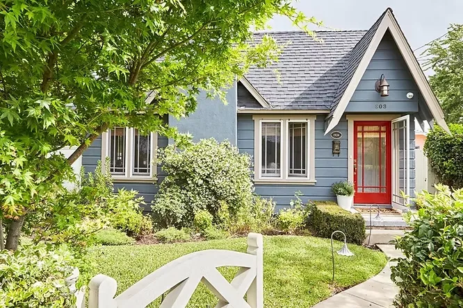 Charming suburban cottage utilizing a vibrant, bright blue siding scheme complemented perfectly by a poppy red front door.