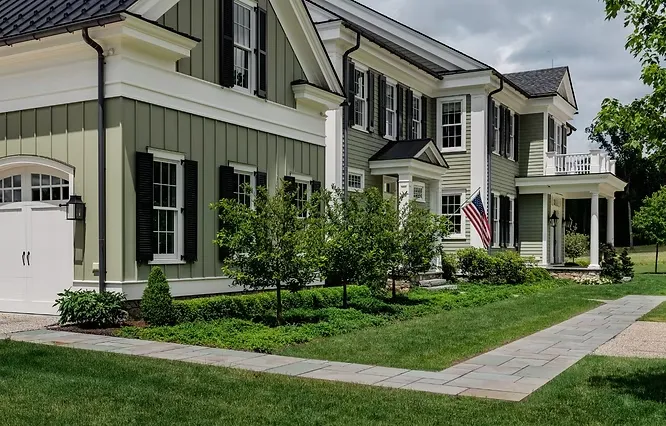 Elegant colonial-style house painted in a calming sage green hue with crisp white trim and traditional black shutters.