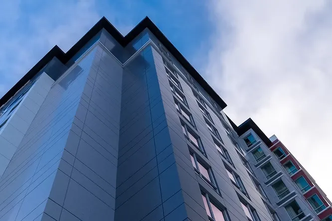 Modern high-rise apartment building featuring sleek, blue-toned reflective metal cladding against a cloudy sky.