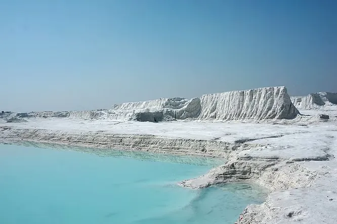 The surreal white landscape of the Kishangarh marble slurry dumping yard frames an unexpectedly vibrant, turquoise lake.