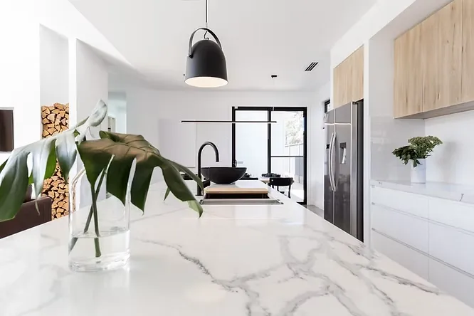 Bright modern kitchen island topped with elegant Carrara marble featuring soft gray veins, accented by a black pendant lamp.