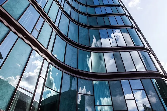 Striking curved skyscraper facade composed of reflective blue glass panels mirroring a bright, cloudy sky.