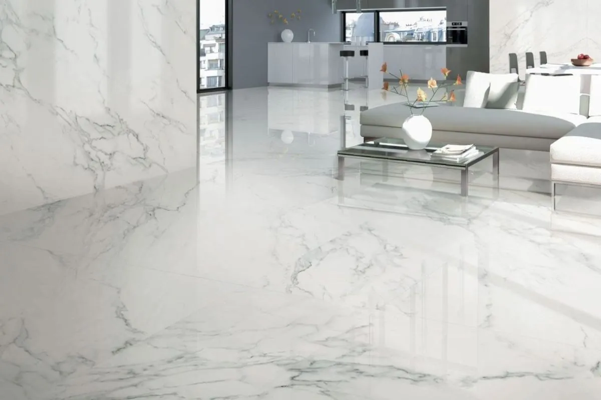 A close-up shot of white Italian marble flooring in a well-lit room, showcasing its seamless, polished surface and subtle grey veining.