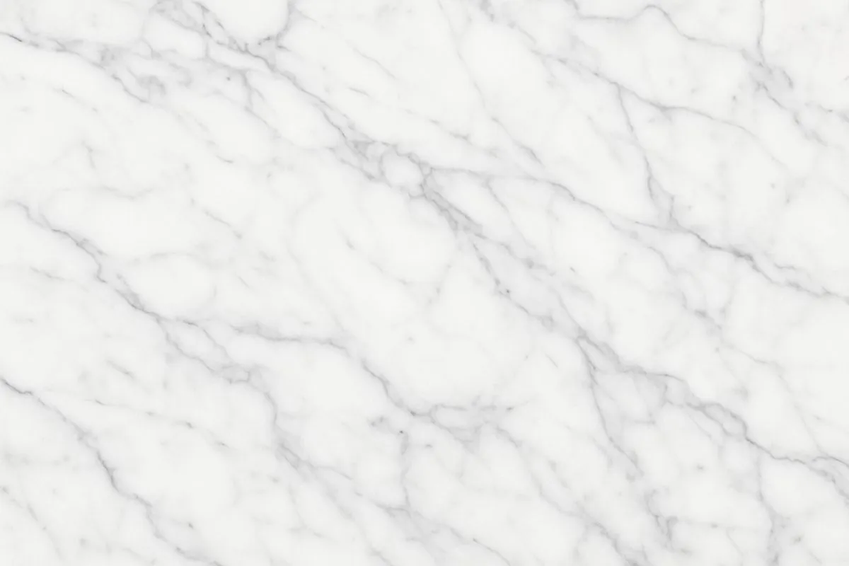 A close-up view of Carrara marble, showing its distinctive white surface with fine, delicate grey veins running across the stone.