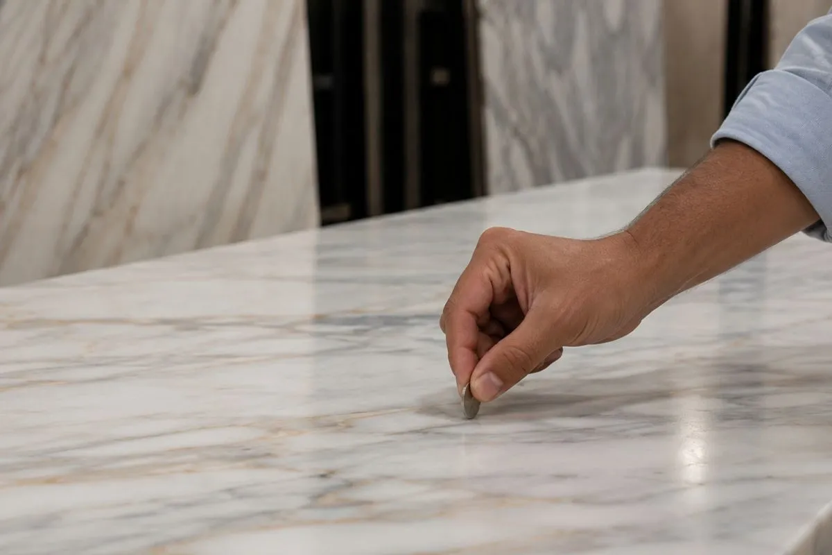 A close shot of a hand tapping a coin on a shiny Kitchen Marble Slab to check it.
