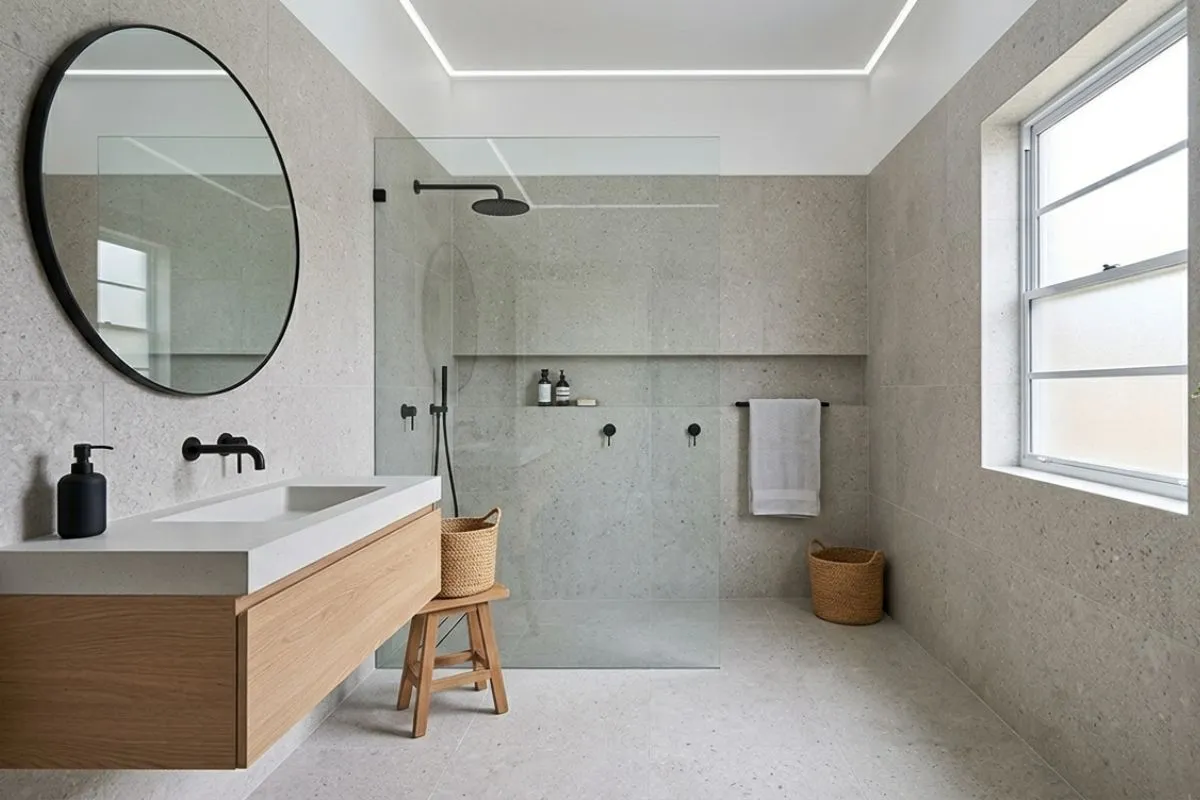Spacious bathroom interior featuring light terrazzo tiles, a round mirror, and a walk-in shower.