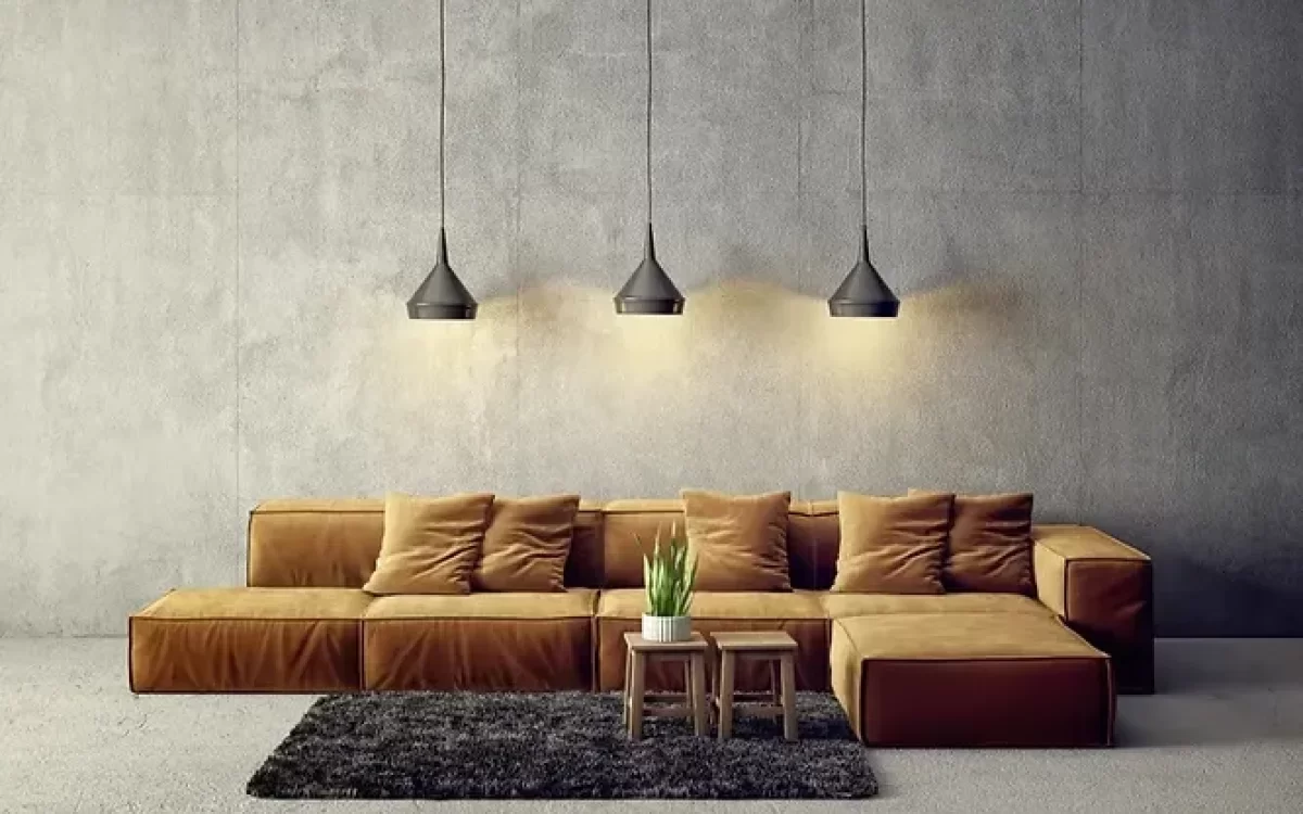 Three black modern pendant lights hanging over a long brown couch against a textured grey concrete wall.