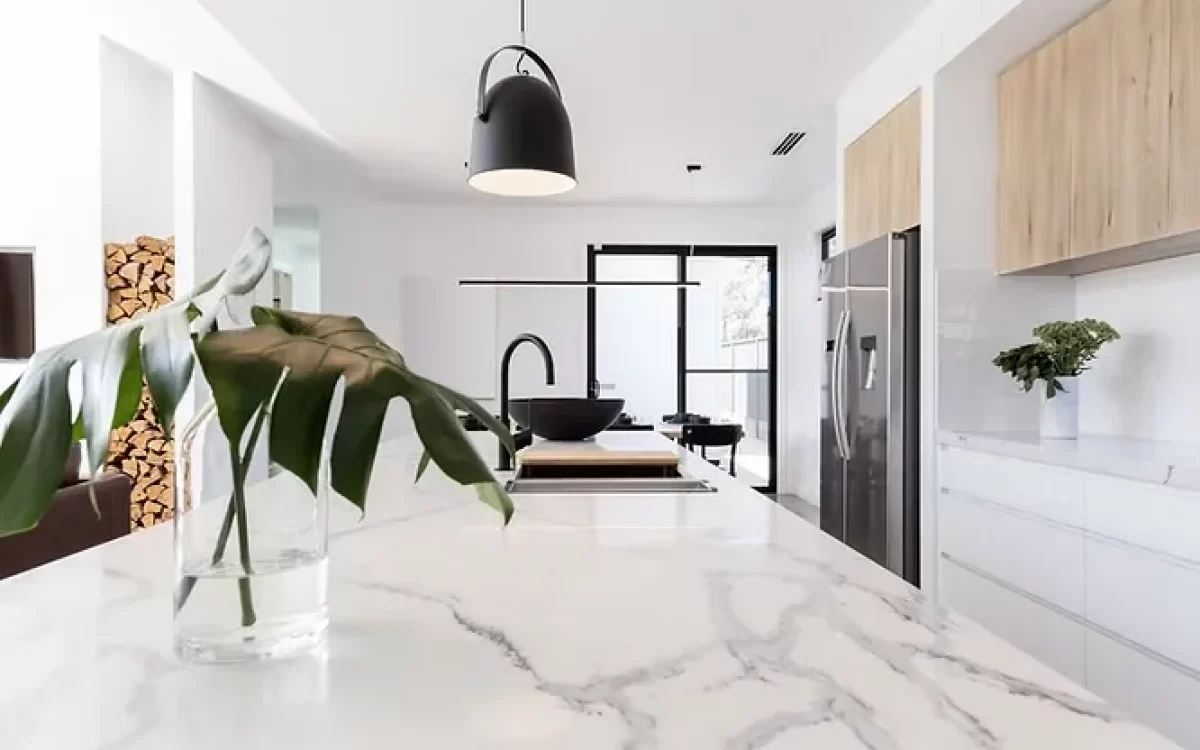 Bright modern kitchen island topped with elegant Carrara marble featuring soft gray veins, accented by a black pendant lamp.