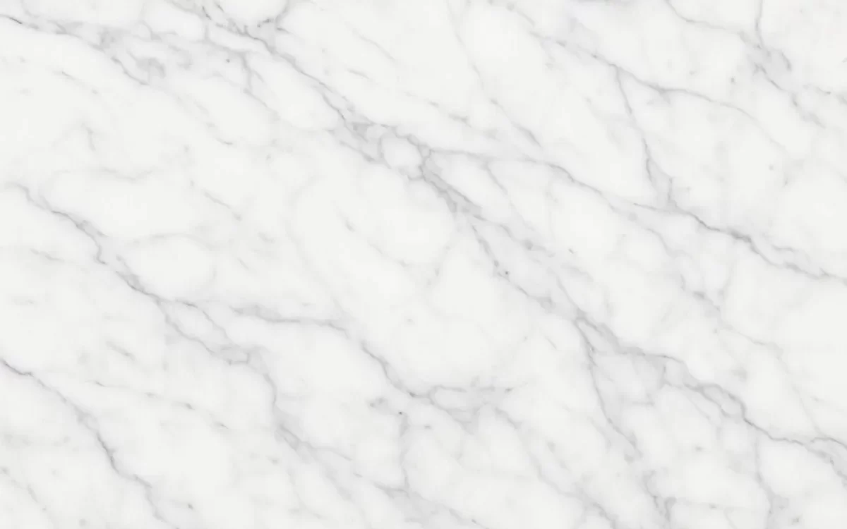 A close-up view of Carrara marble, showing its distinctive white surface with fine, delicate grey veins running across the stone.