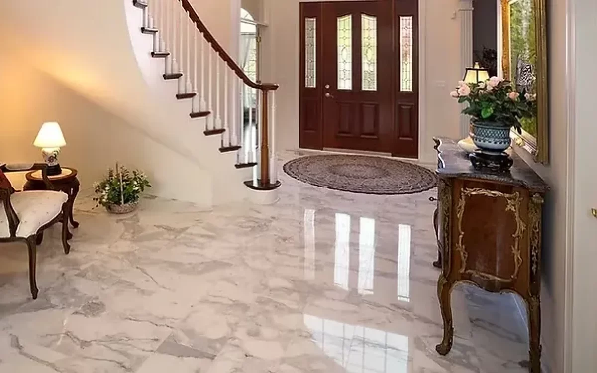 A classic, elegant home foyer showcasing highly polished white marble flooring with grey veining that reflects the warm indoor lighting.