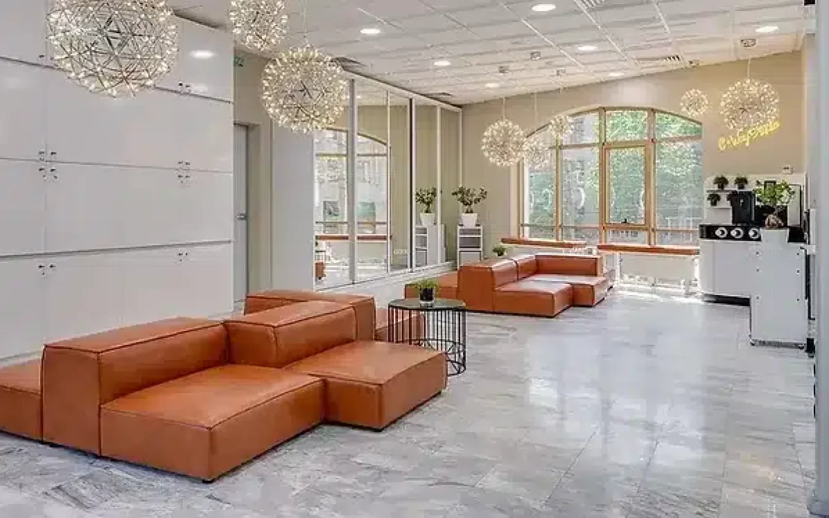A spacious lobby with grey marble flooring, brown leather modular couches, and spherical wire lights.